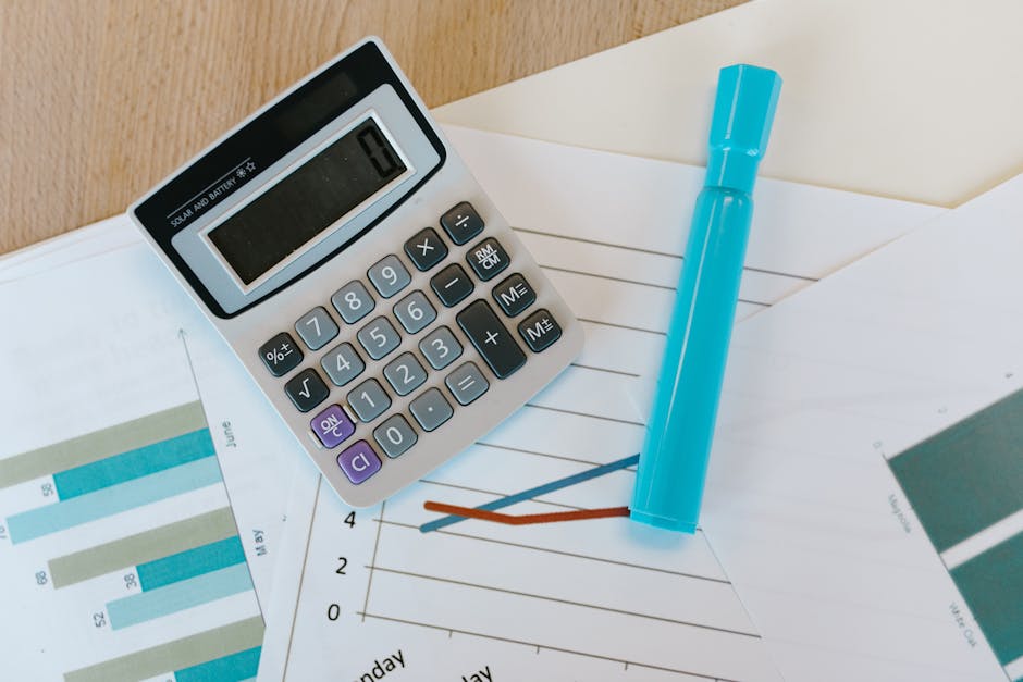 Top view of a calculator and charts on a wooden office desk with a blue marker.